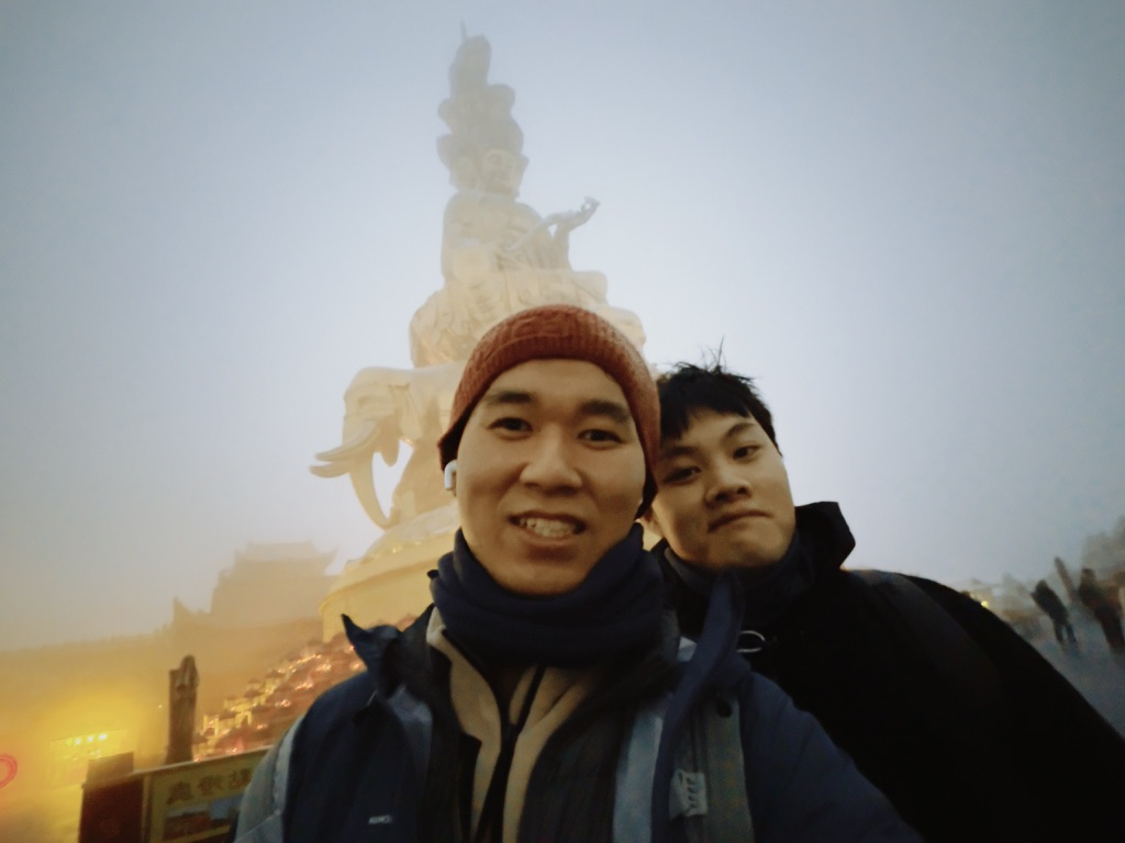 与朋友在峨眉山合影，身后是雾中的山顶雕像